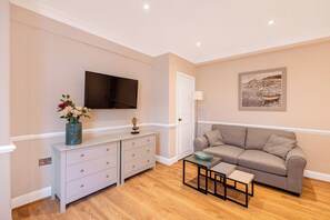 A living room with a sofa, a coffee table, a TV, a cabinet, and a painting on the wall. - Light-filled Studio in Prestigious Chelsea (London)