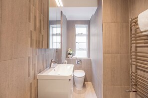 A modern bathroom with a large sink, toilet, and a window providing natural light. - Light-filled Studio in Prestigious Chelsea (London)