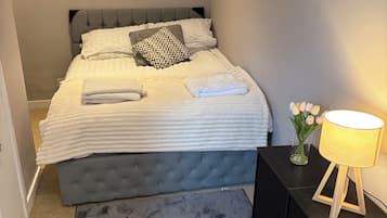 A neatly made bed with pillows, a bedside table with a lamp, and a rug.