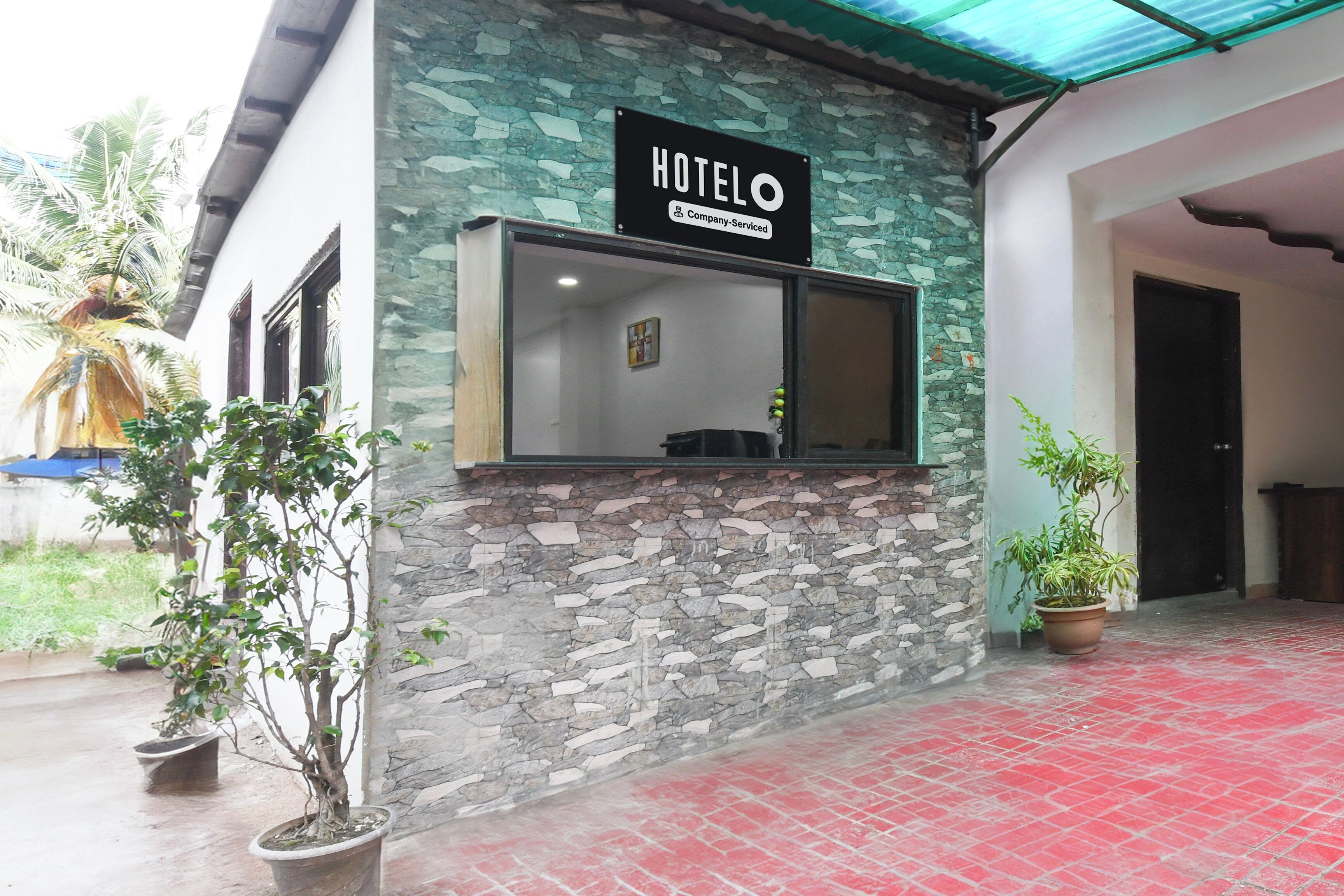 Exterior de un hotel con fachada de piedra, un letrero que indica que es un hotel de servicios para empresas, y plantas en macetas.