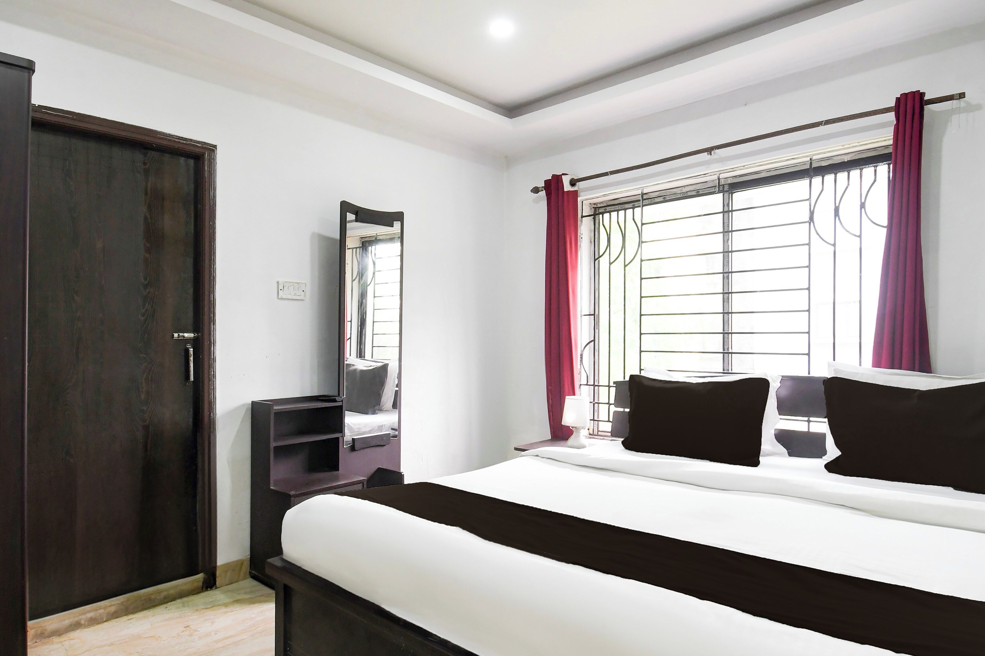 A bedroom with a bed, a wardrobe, a mirror, and a window with curtains.