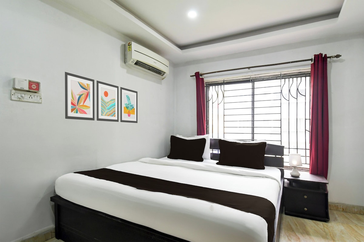 A hotel room with a bed, a bedside table, a window with curtains, and wall-mounted artwork.