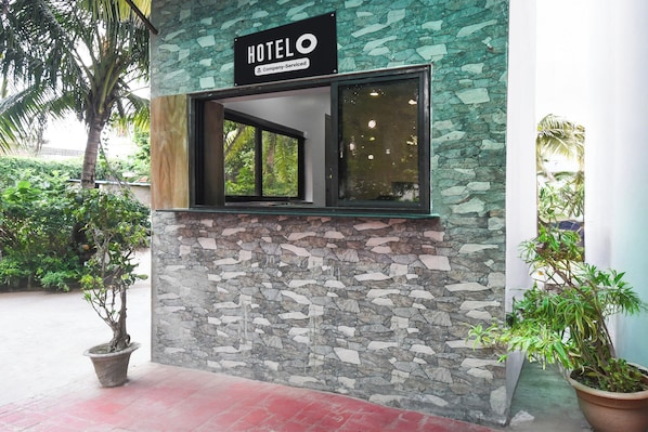 A hotel exterior with a stone facade, a sign indicating it is company-serviced, and a window with a view of greenery.