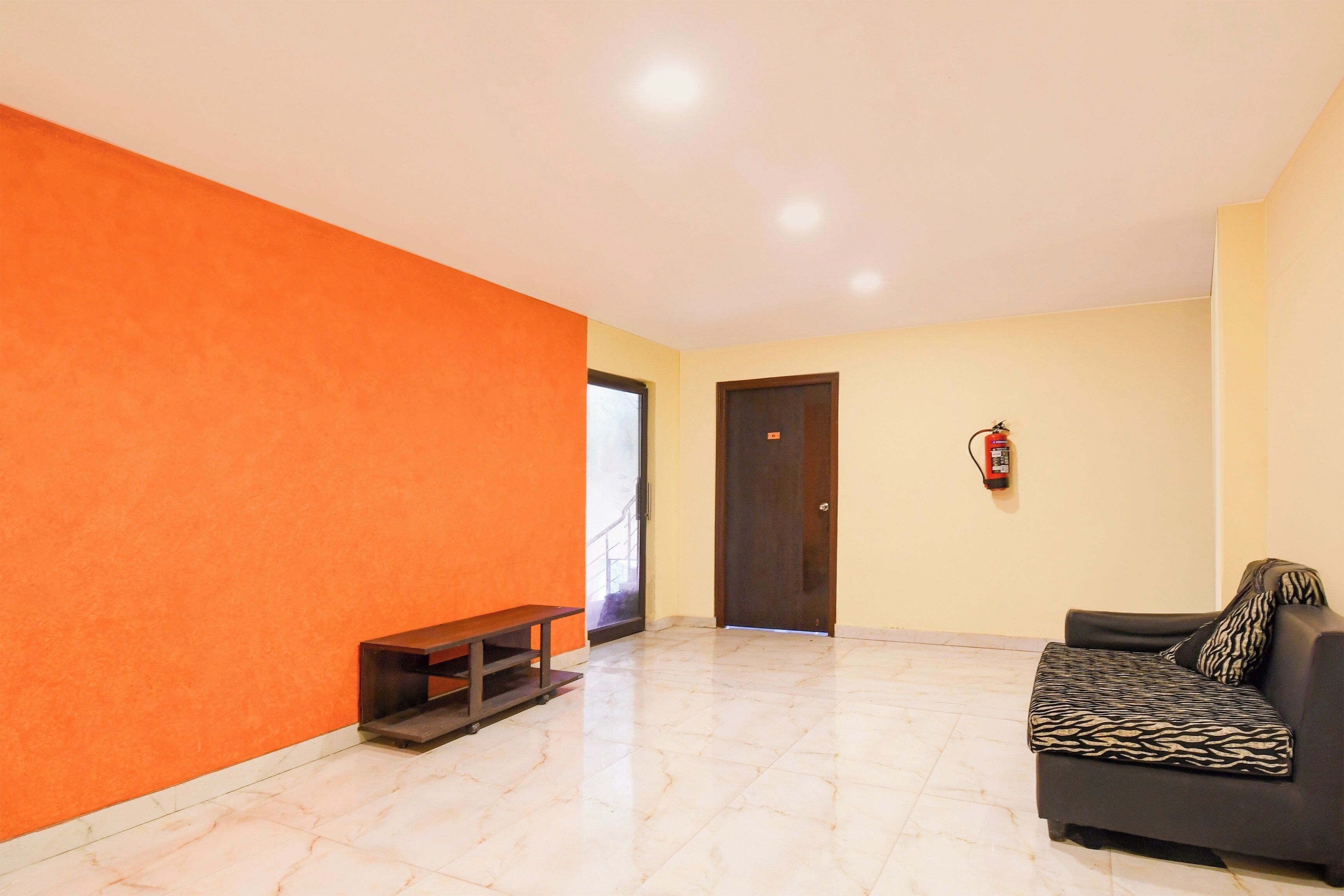 Una habitación con sofá, banqueta, puerta y extintor.