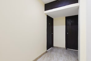 Un pasillo estrecho con dos puertas oscuras, una pared de color claro y un suelo de baldosas.