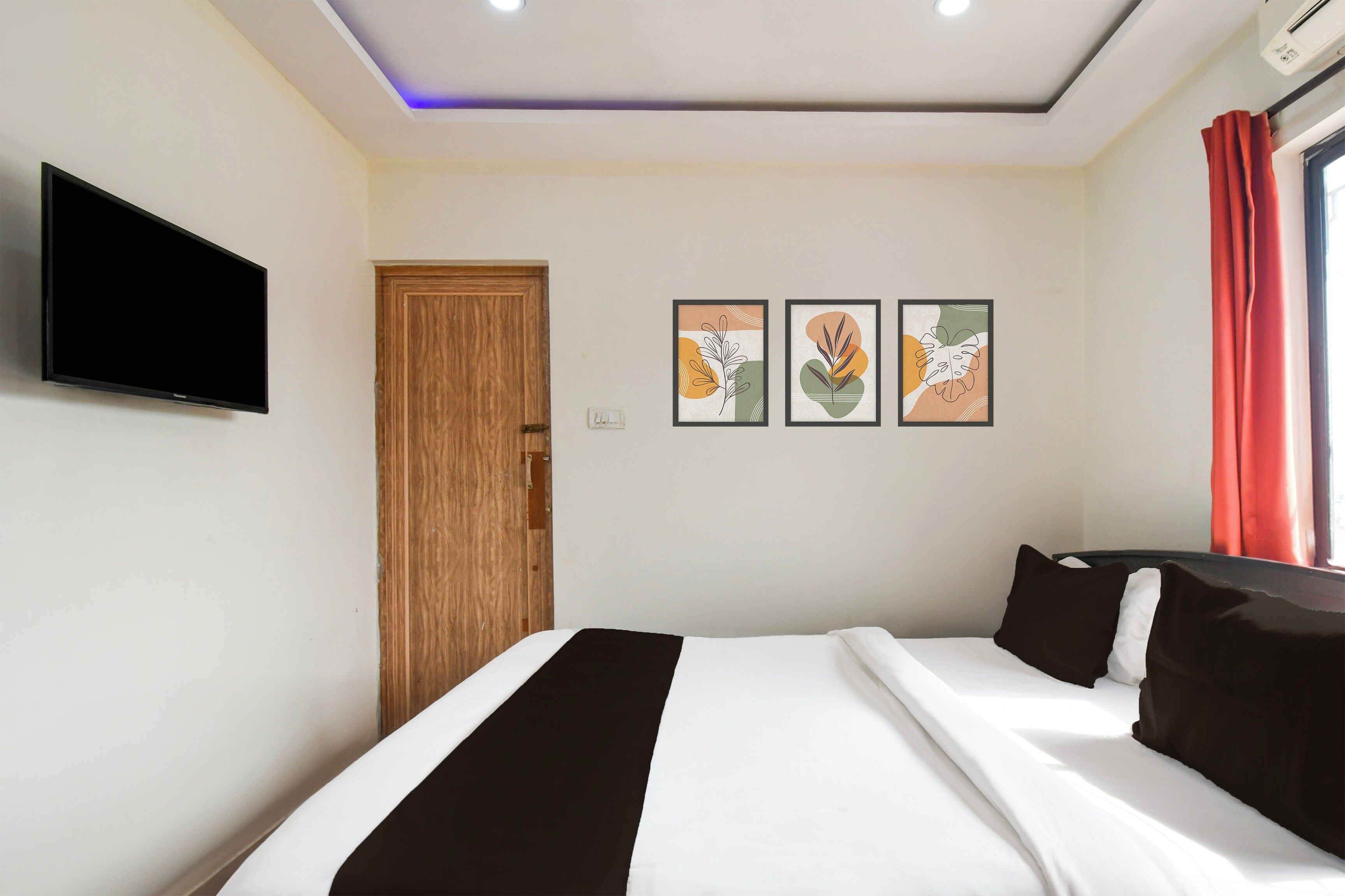 Una habitación de hotel con una cama, un televisor montado en la pared y dos cuadros enmarcados.