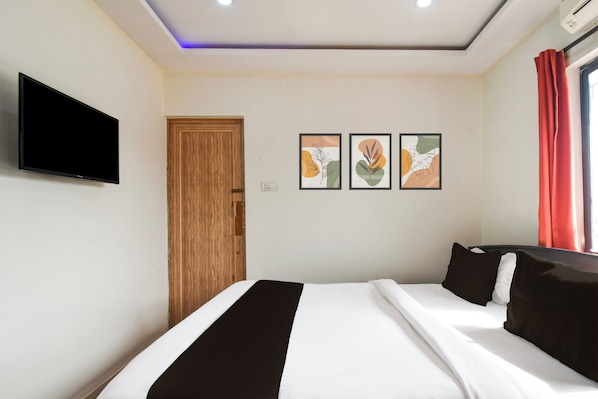 A hotel room with a bed, a television mounted on the wall, and two framed artworks on the wall.