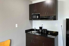 A compact kitchen with dark cabinets, a microwave, a coffee maker, and a sink. - 1 Queen Bed | Non-Smoking, Kitchen (Abilene)