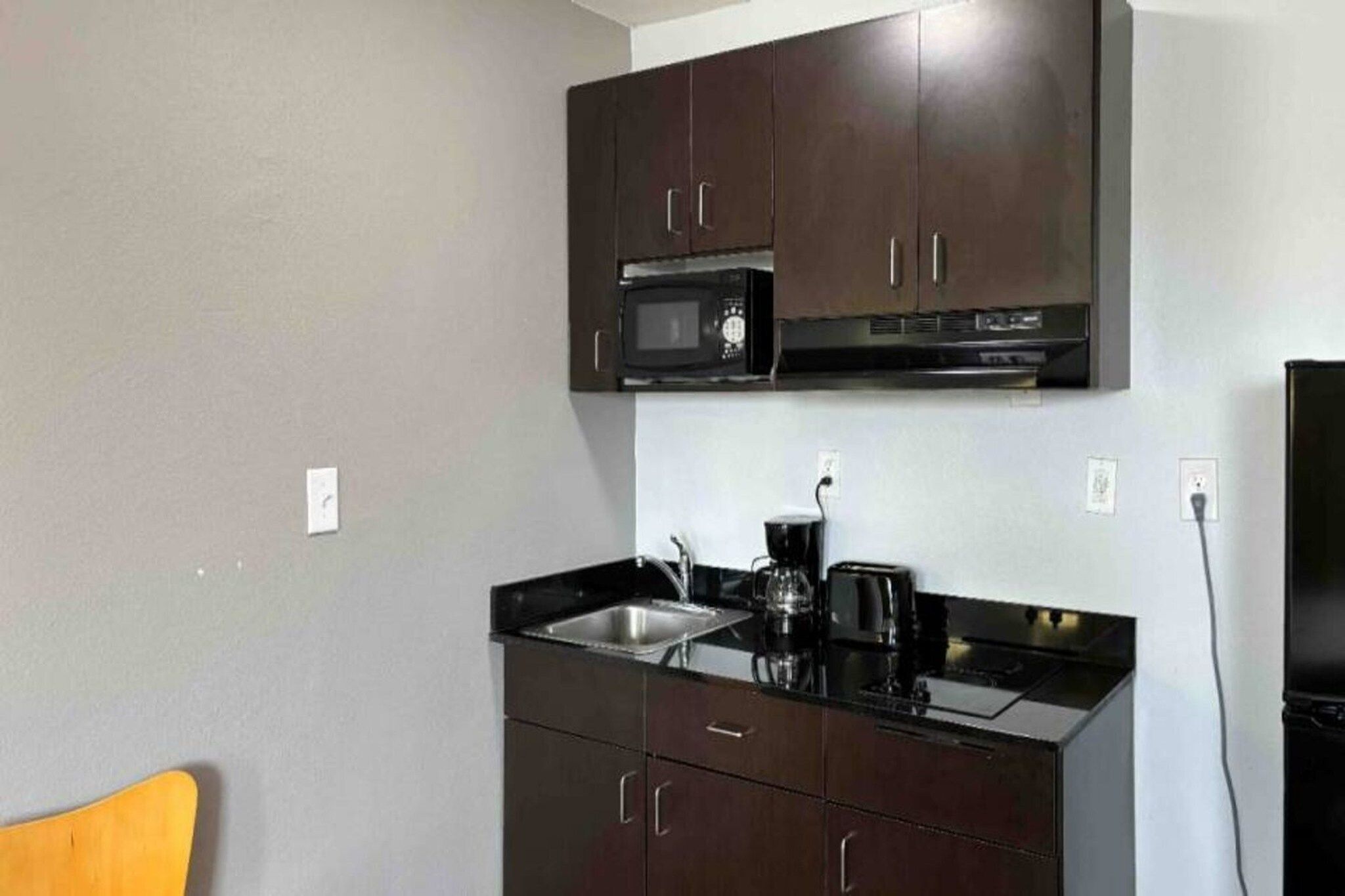A compact kitchen with dark cabinets, a microwave, a coffee maker, and a sink.