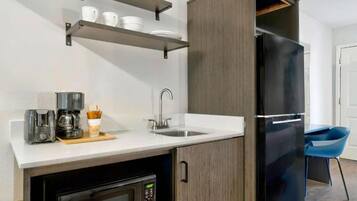A compact kitchen with a refrigerator, coffee machine, and a microwave.