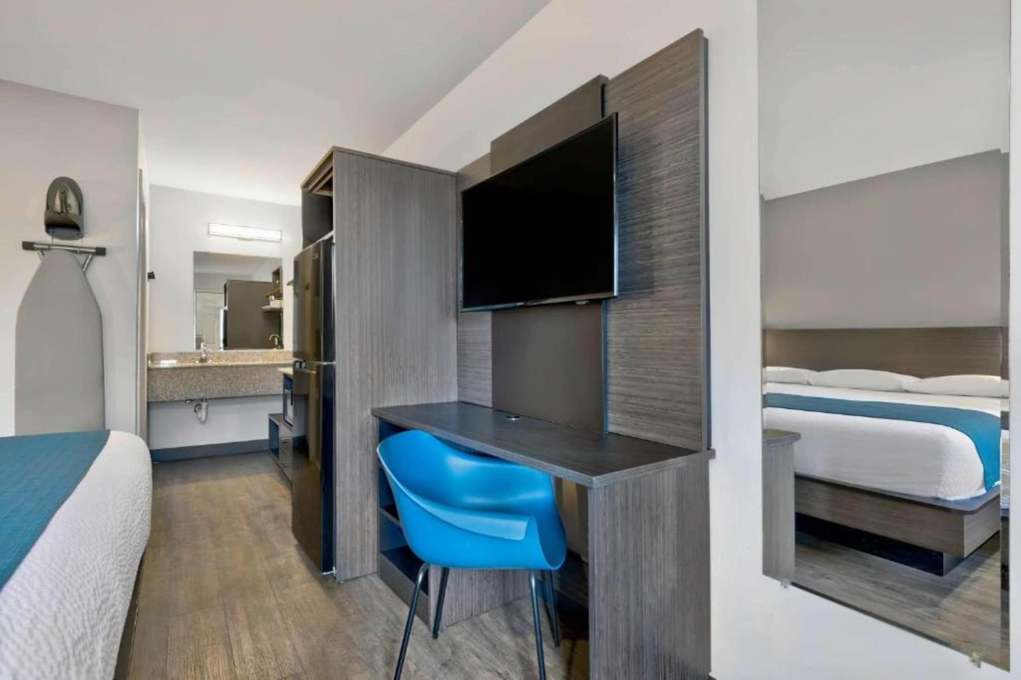 A hotel room with a bed, a desk, a chair, a television, and a mirror.