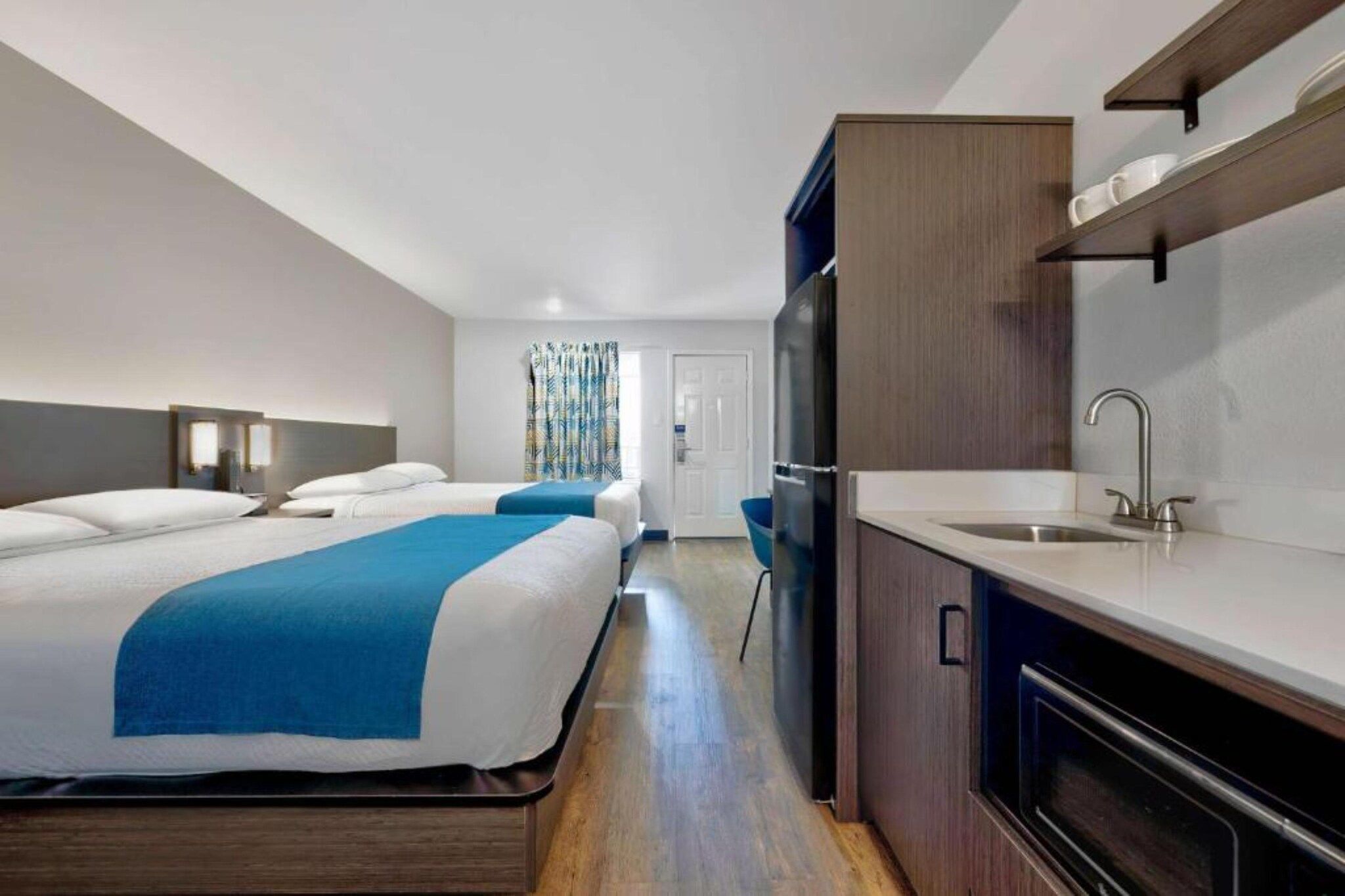 A hotel room with two beds, a kitchenette, and a bathroom.