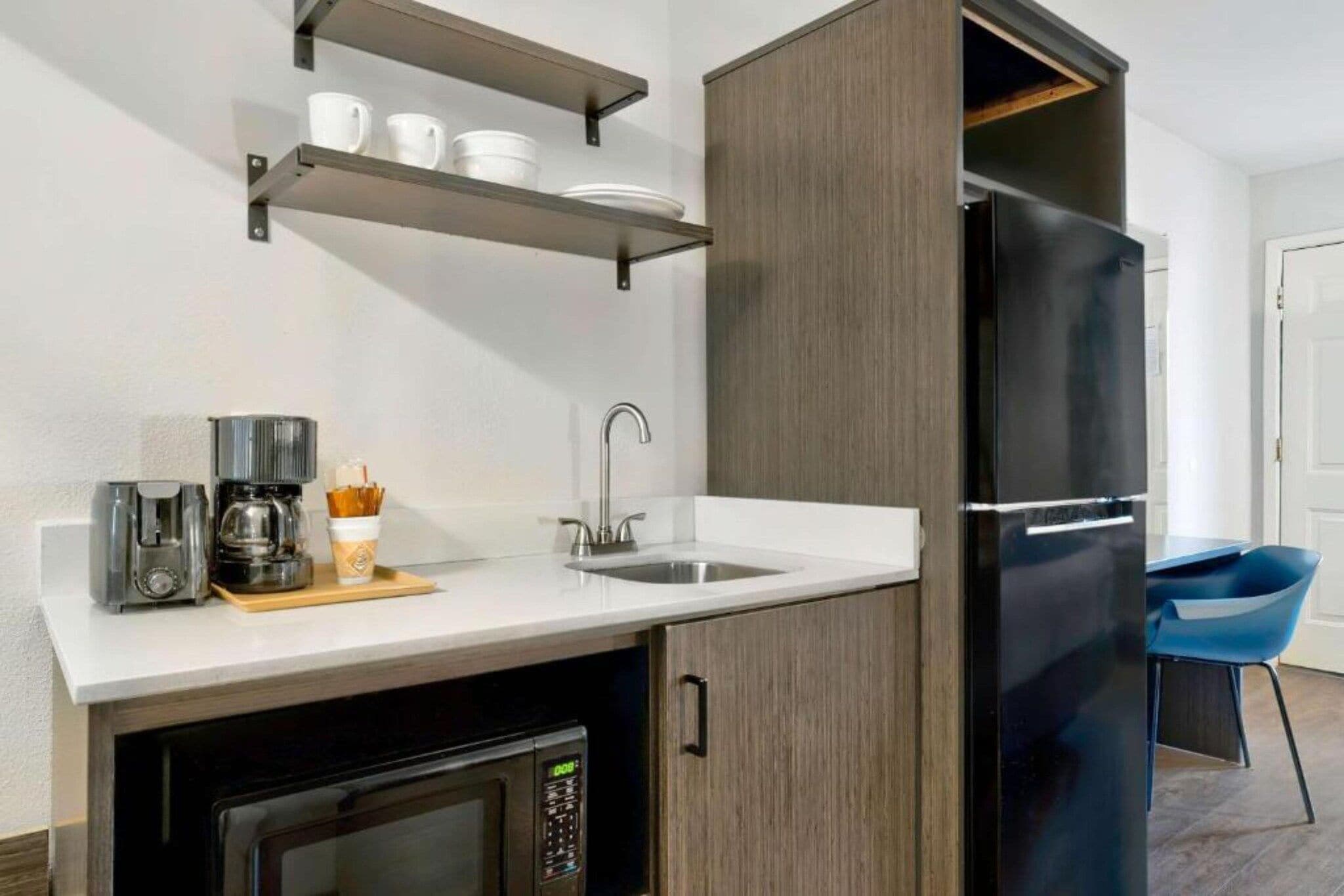 A compact kitchen with a refrigerator, coffee machine, and a microwave.