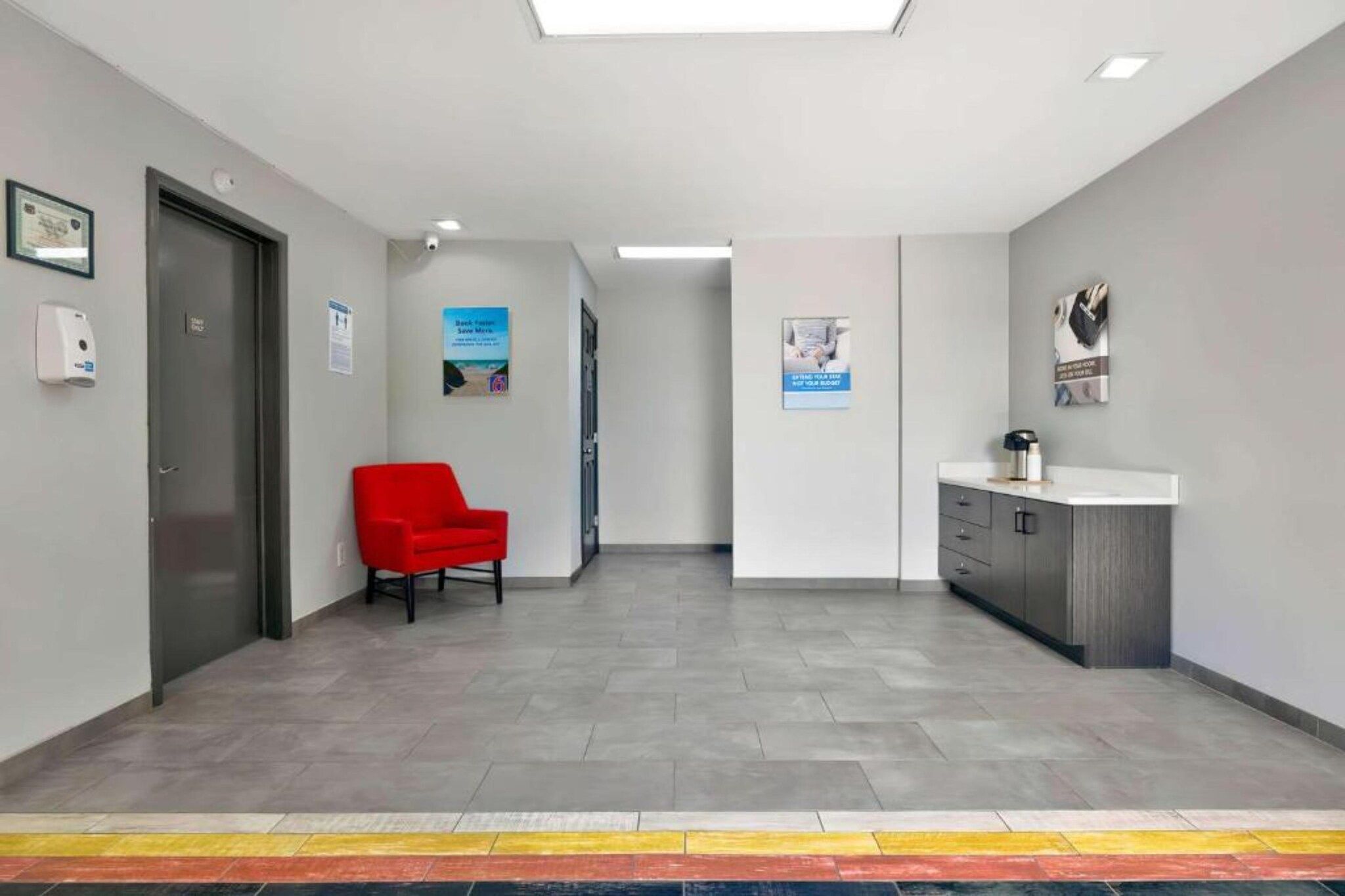 A modern waiting area with a red chair, a reception desk, and a door.