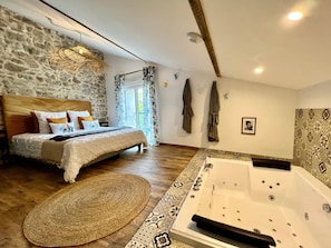Quarto com cama, uma janela grande, parede de pedra, banheira e tapete estampado.