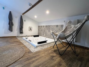 Quarto com piso de madeira, uma banheira grande, parede estampada e uma cadeira.