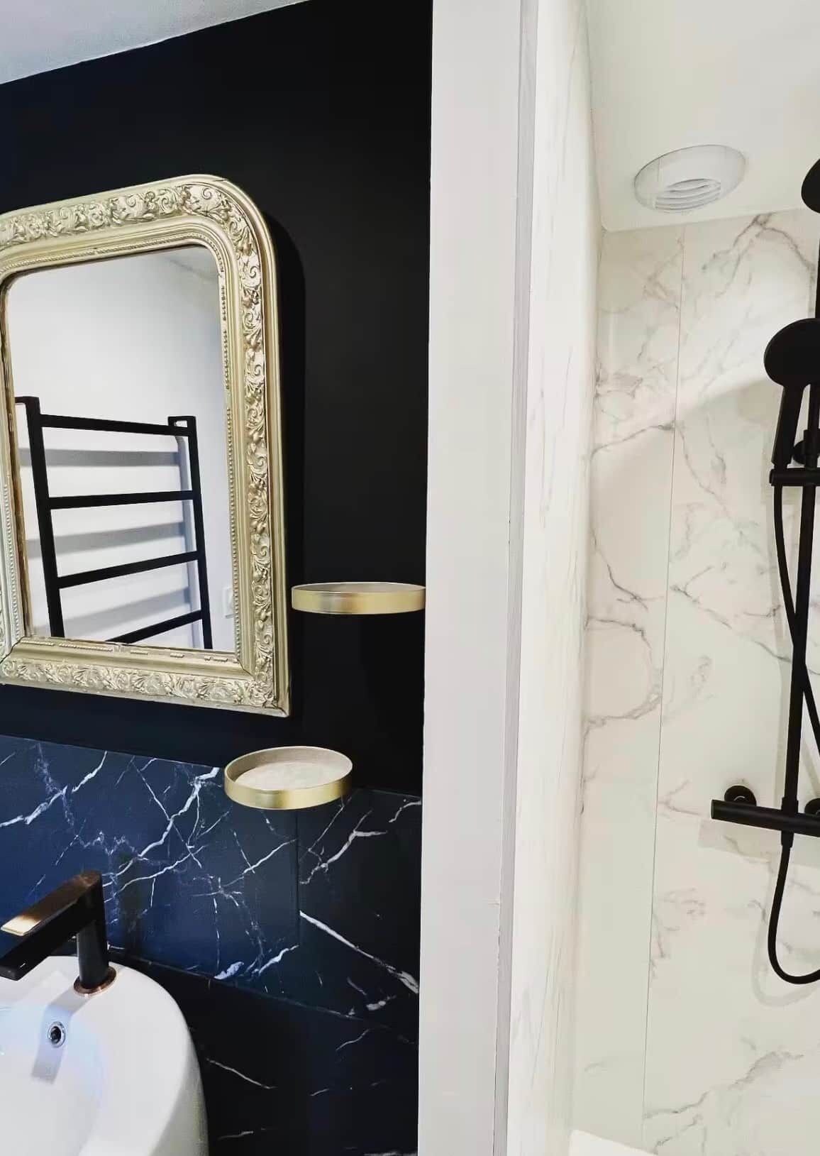 Een badkamer met een zwart wastafel, een spiegel met gouden lijst en een douche met een marmeren wand.