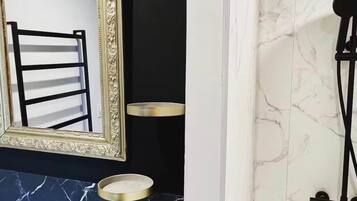 Een badkamer met een zwart wastafel, een spiegel met gouden lijst en een douche met een marmeren wand.