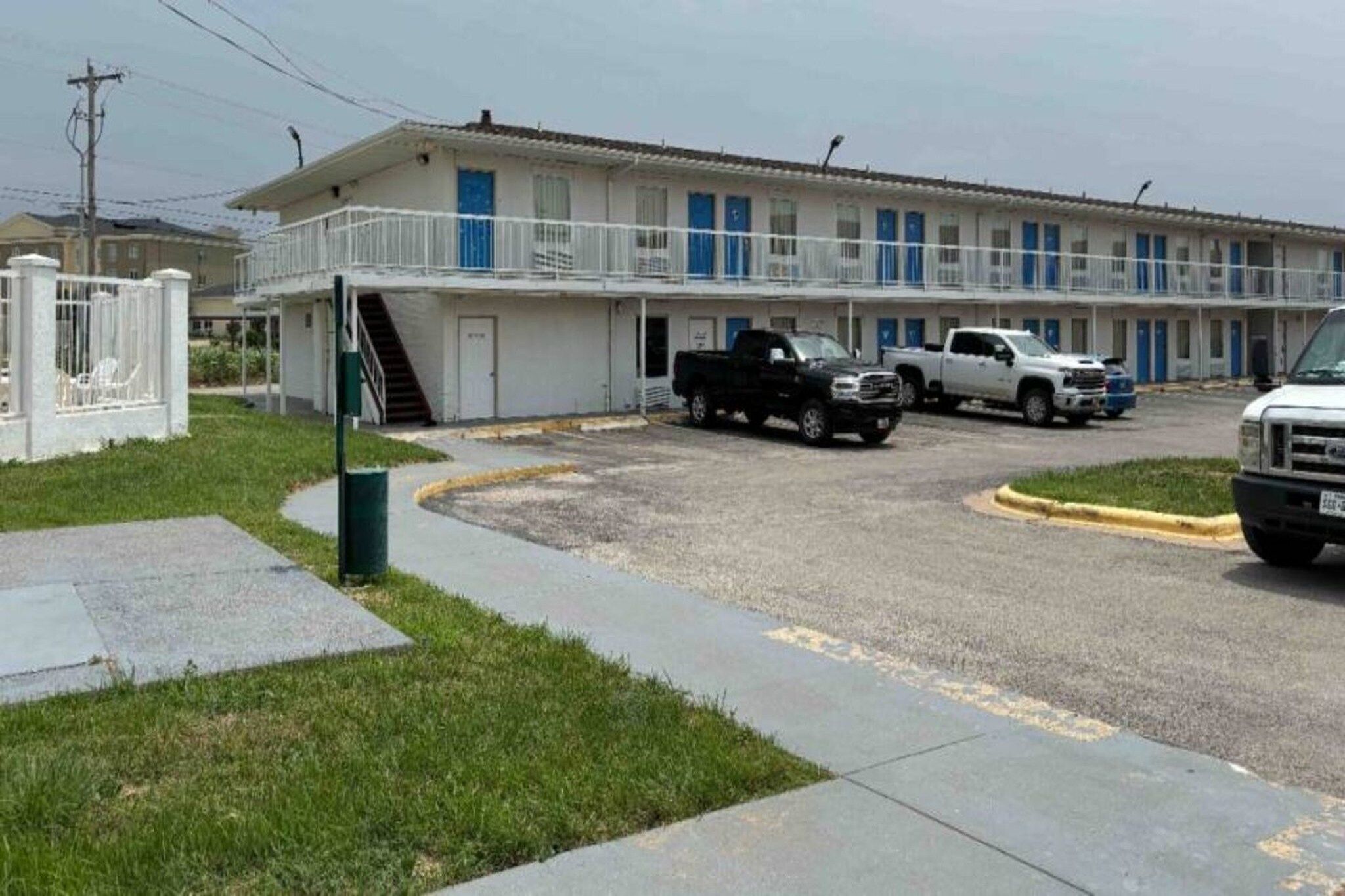 A motel with a parking area, a covered walkway, and a building with multiple windows.