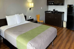 Ein Hotelzimmer mit einem Bett, einem Sessel, einer Küchenzeile und einem Mülleimer.