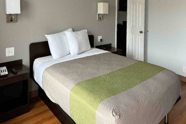 A hotel room with a bed, bedside tables, a nightstand, and a door.