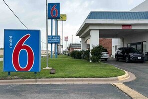 Un motel avec un grand panneau indiquant le chiffre « 6 », une station-service avec un panneau indiquant « SOLDES – 12 » et un panneau indiquant « CUISINE AMÉNAGÉE – TV HD 50 »