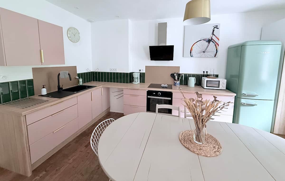 A modern kitchen with a white table, pink cabinets, and a green refrigerator.