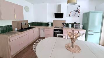 A modern kitchen with a white table, pink cabinets, and a green refrigerator.