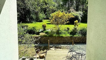 Een terras met tuinmeubilair, een kleine tuin met een vijver en uitzicht op een bebost gebied.