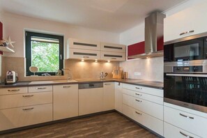 A modern kitchen with white cabinetry, a stainless steel range hood, and a built-in oven. - Holiday apartment with 2 bedrooms (Sassnitz auf Rügen)