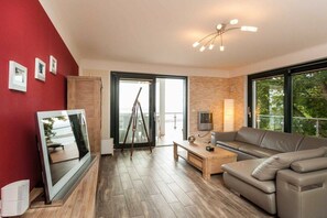 Ein modernes Wohnzimmer mit großem Fenster, einer Couch, einem Couchtisch und einem Flachbildfernseher.