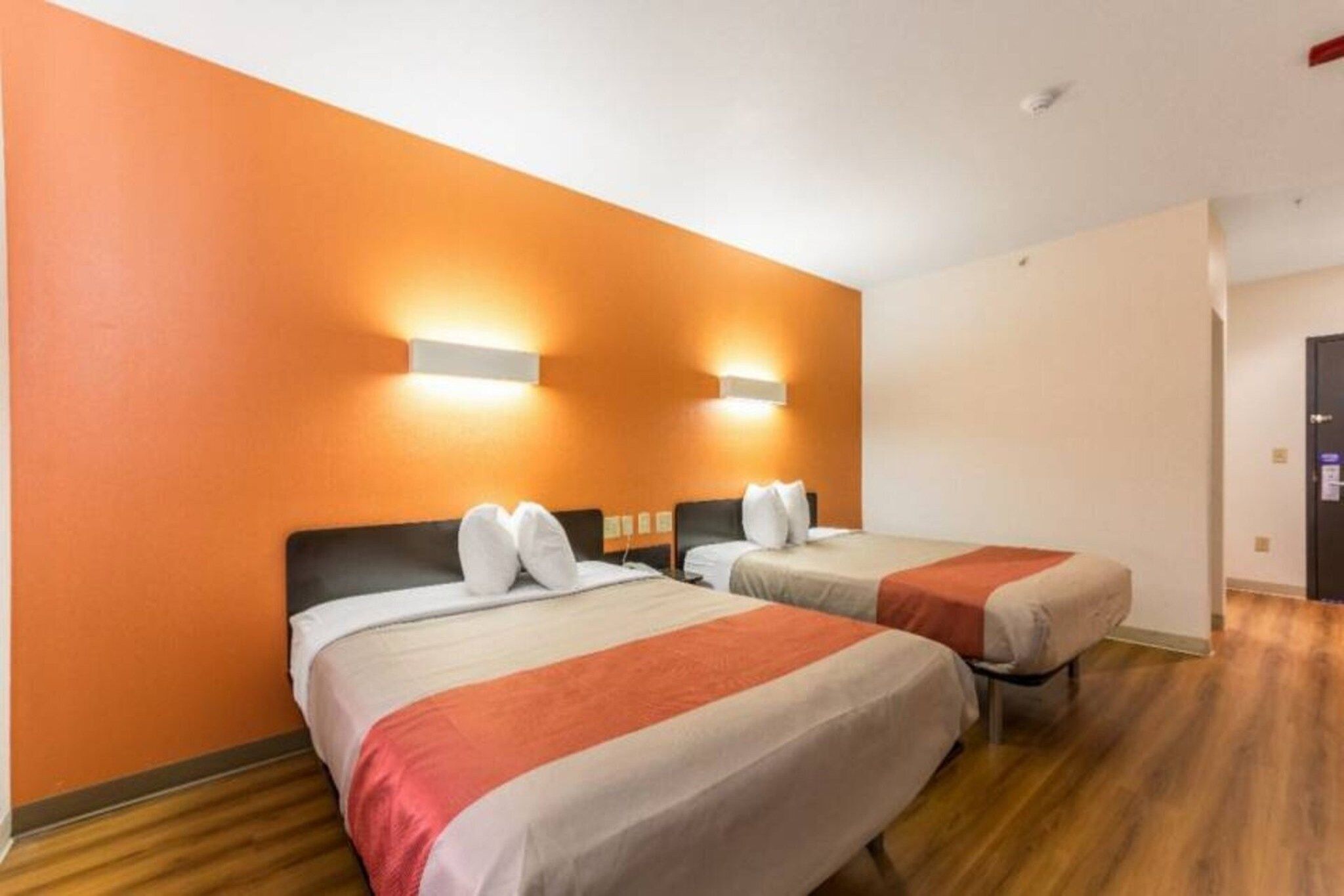 Habitación de hotel con dos camas, piso de madera y paredes color naranja.