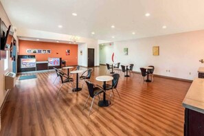A hotel lobby with a reception desk, several tables and chairs, and a wooden floor.