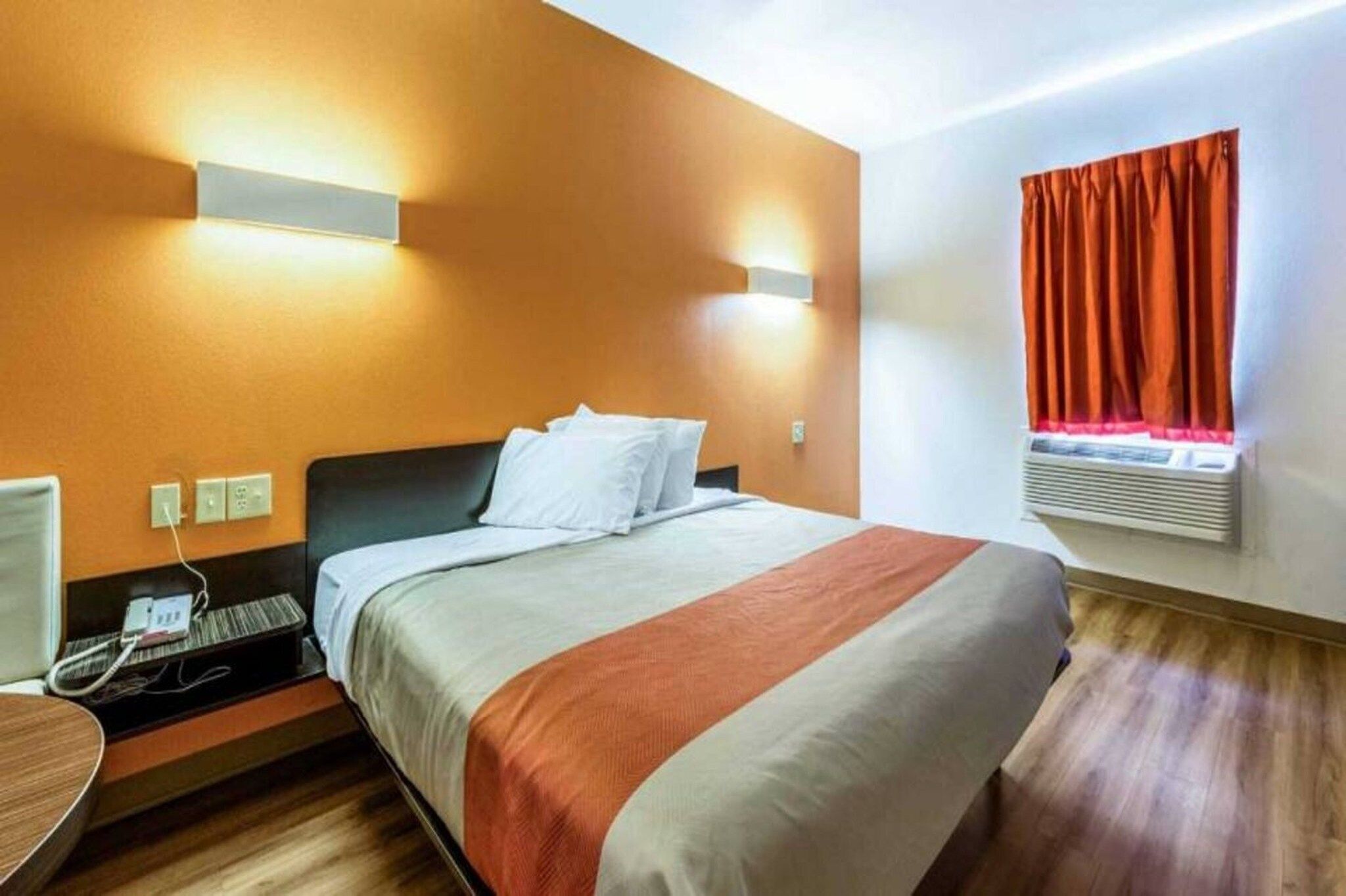A hotel room with a bed, bedside table, and a wall-mounted heater.