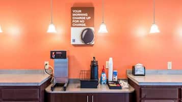 Zona de recepción de un hotel con una máquina de café, una balanza y un cartel que indica cargo matutino gratuito.