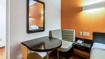 Una habitación de hotel con una cama, una mesita de noche, una silla, una pequeña mesa, un espejo y un teléfono en la pared.