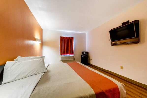 A hotel room with a bed, a television, and a window with curtains.
