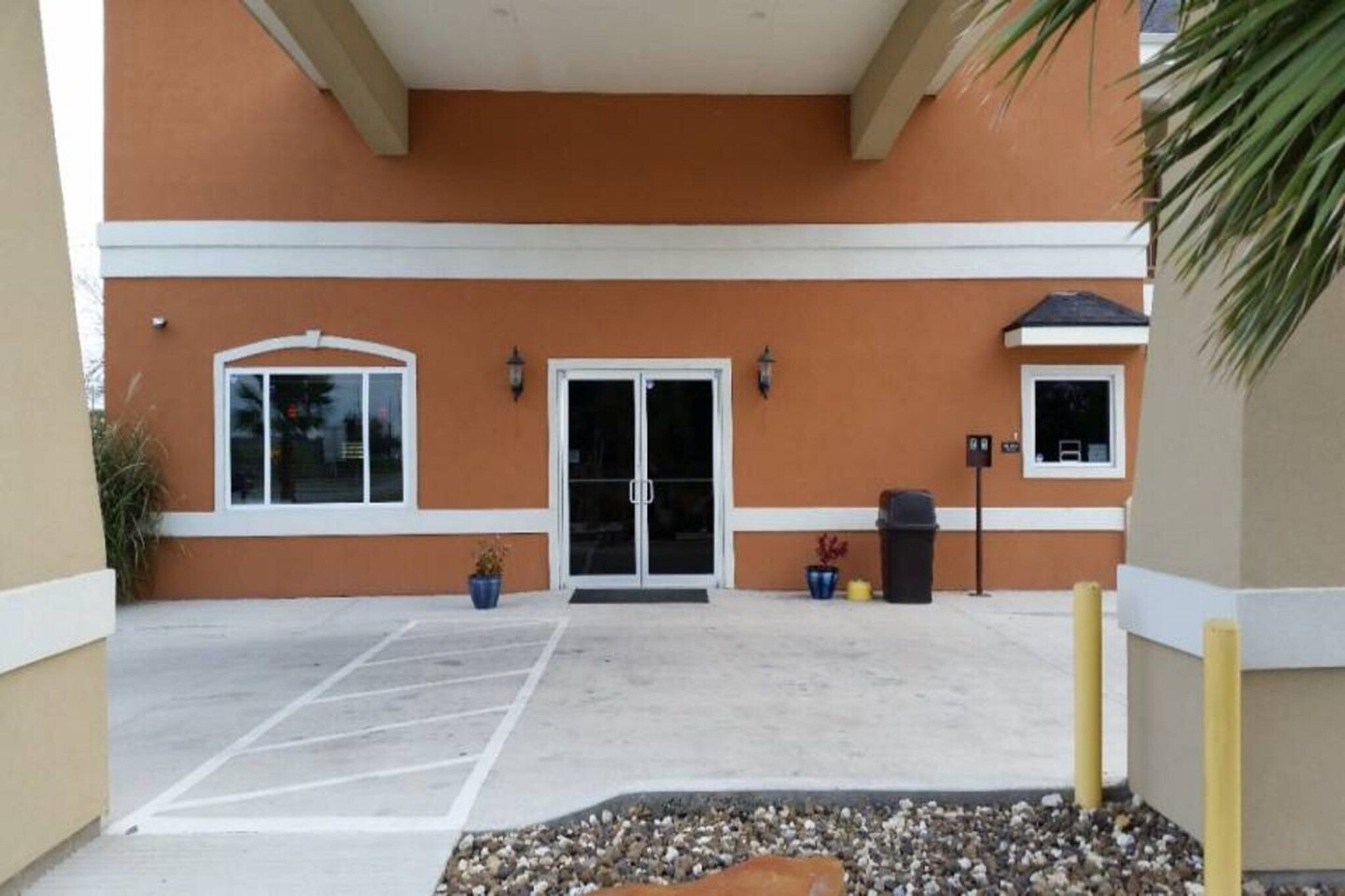 A building entrance with a parking lot, double doors, and potted plants.