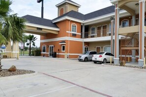 A multi-story hotel with a parking lot, a covered entrance, and a staircase leading to an upper level.