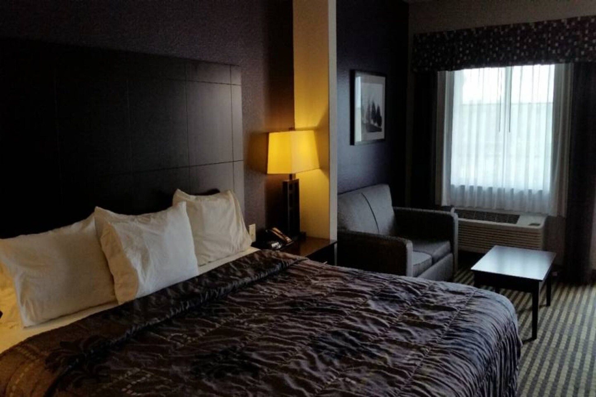 A hotel room with a large bed, a desk, a chair, a lamp, and a window with curtains.