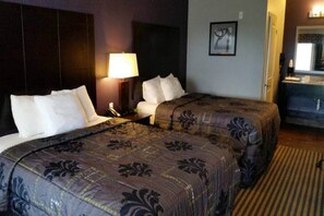 Habitación de hotel con dos camas, una mesita de noche con lámpara, cómoda y un cuadro en la pared.