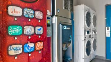 Una lavandería con máquina expendedora que ofrece diversas bebidas y una fila de lavadoras.
