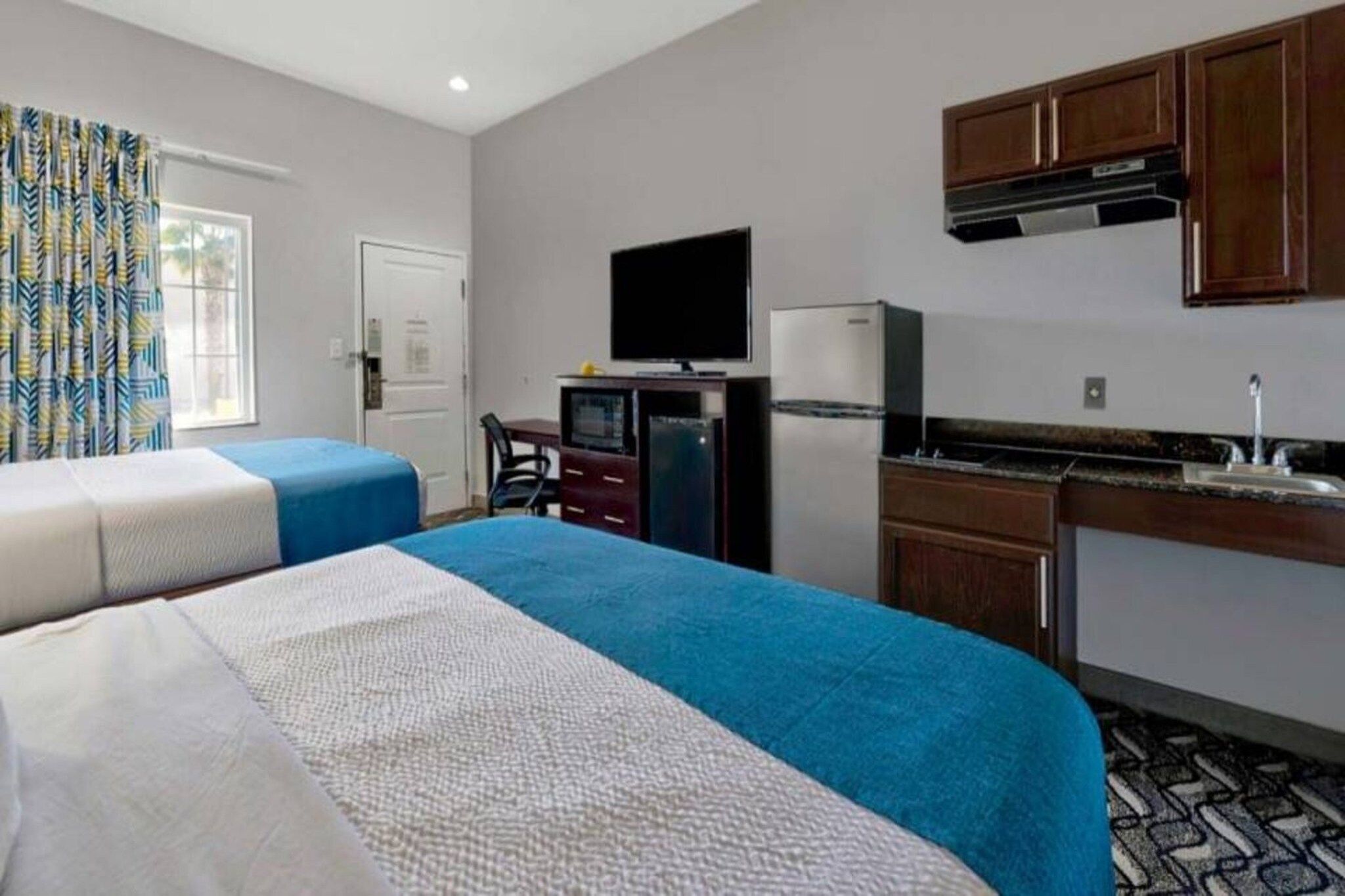 Habitación de hotel con dos camas, televisión, refrigerador, microondas, escritorio pequeño y kitchenette.
