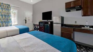 Habitación de hotel con dos camas, televisión, refrigerador, microondas, escritorio pequeño y kitchenette.