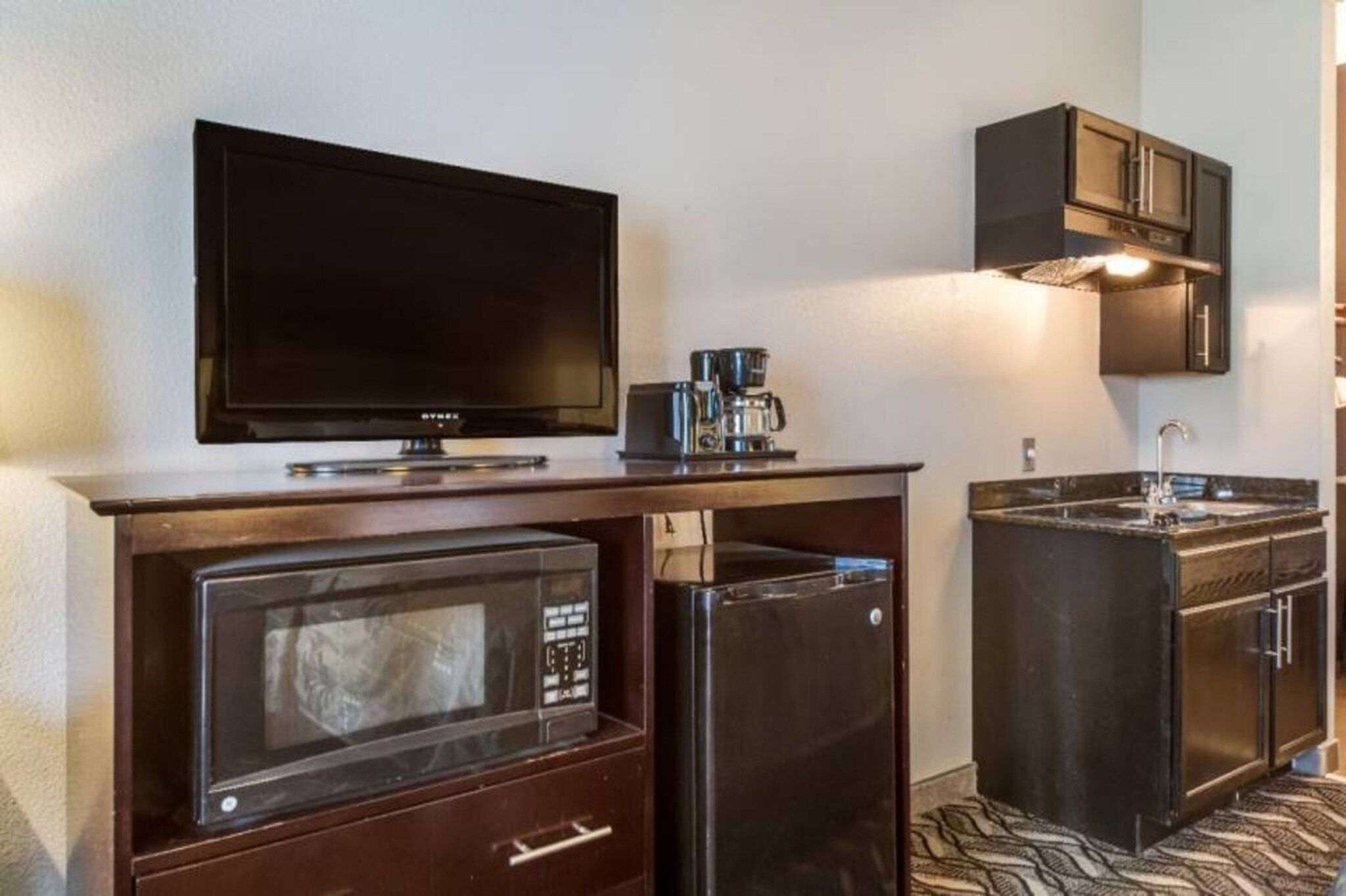 Una kitchenette compacta equipada con microondas, refrigerador, cafetera y un televisor de pantalla plana.