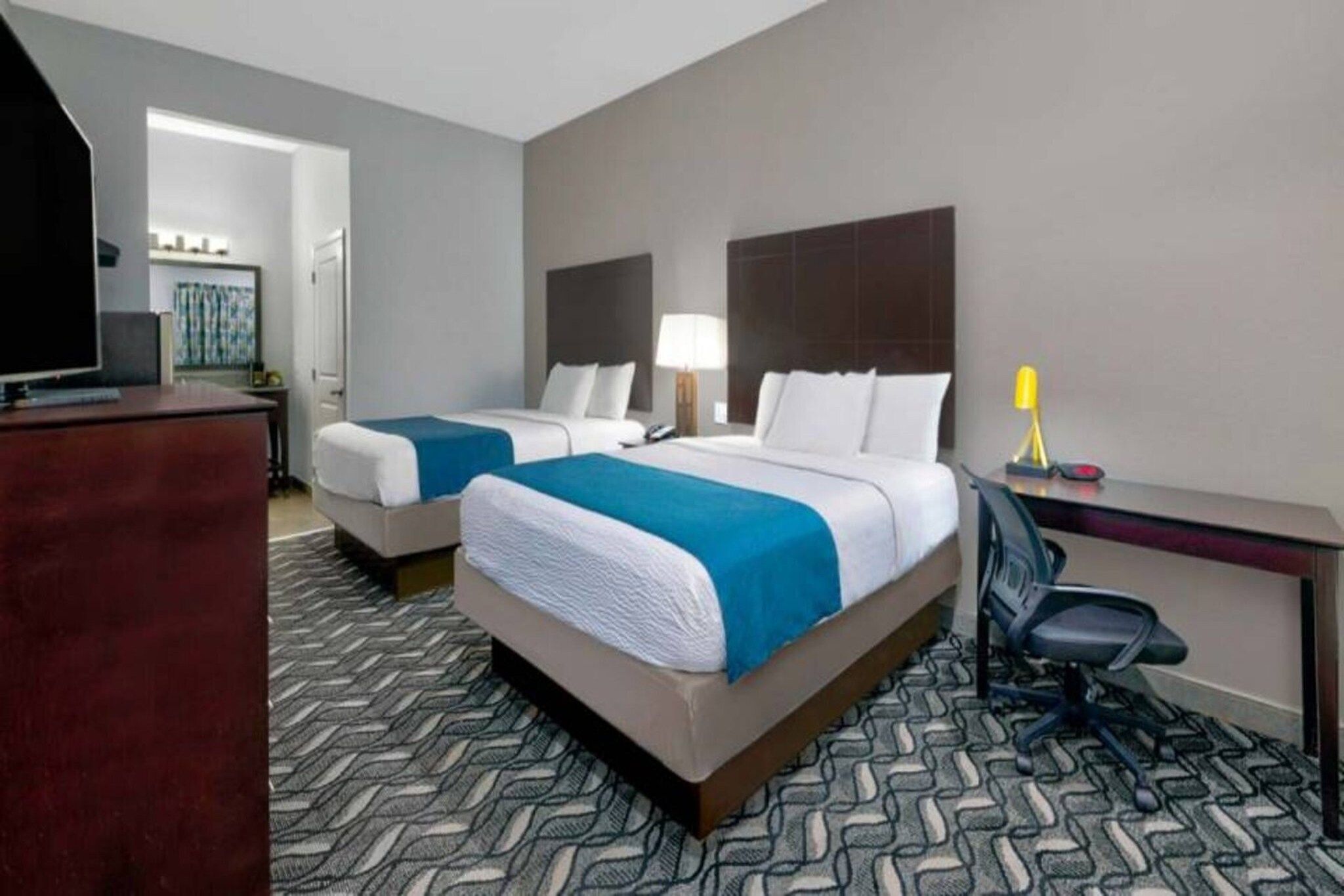 A hotel room with two beds, a desk, a chair, and a television.