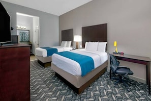 A hotel room with two beds, a desk, a chair, and a television.