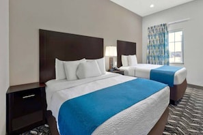 A hotel room with two beds, a nightstand, a lamp, and a window with curtains.