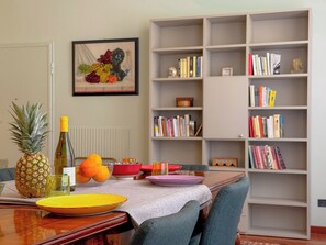 Ein Essbereich mit einem Holztisch, Stühlen, einem Bücherregal und einem gerahmten Kunstwerk an der Wand.