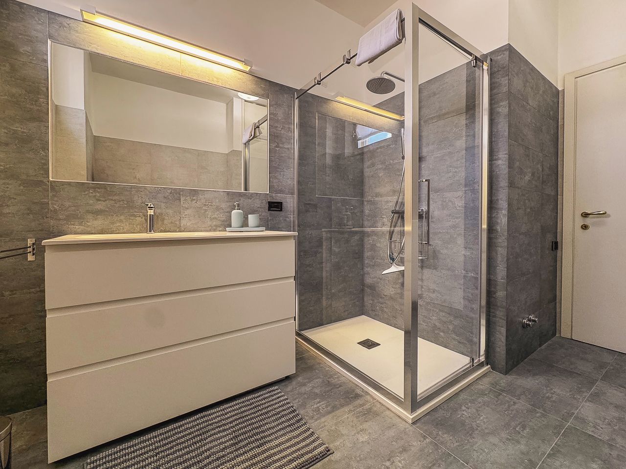 Un baño moderno con ducha envuelta en vidrio, un espejo grande y un tocador con cajones.